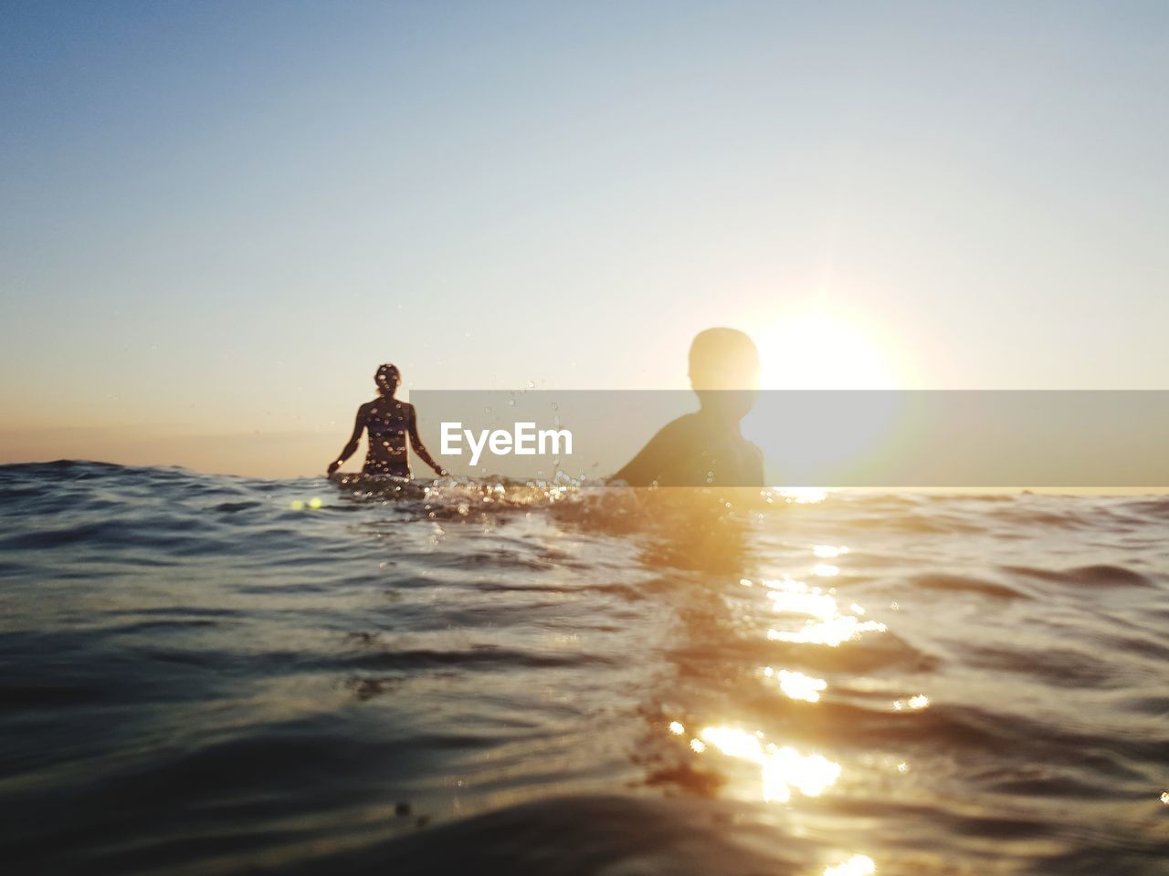 PEOPLE IN SEA AGAINST CLEAR SKY DURING SUNSET