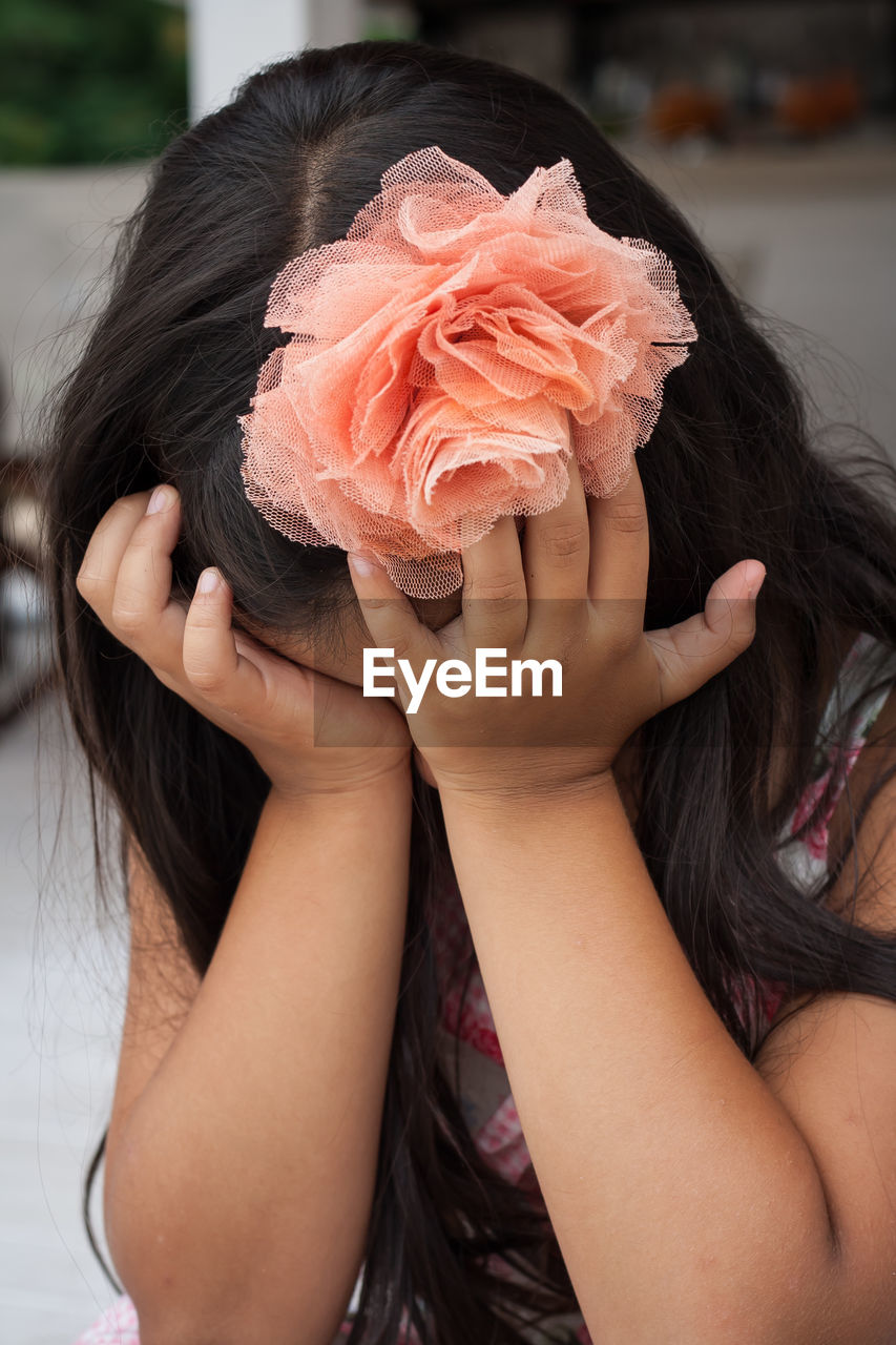 Sad girl wearing artificial flower while covering eyes with hands