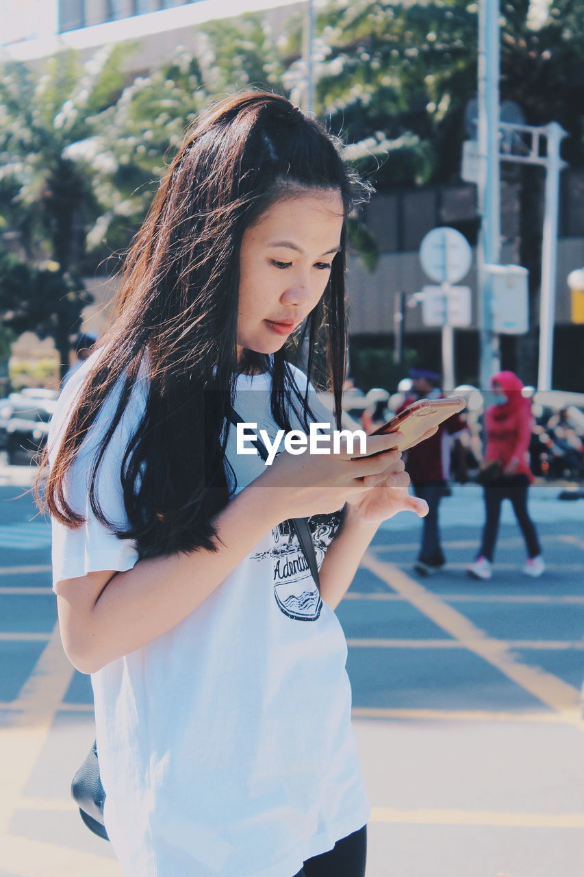 Woman using mobile phone while standing on street