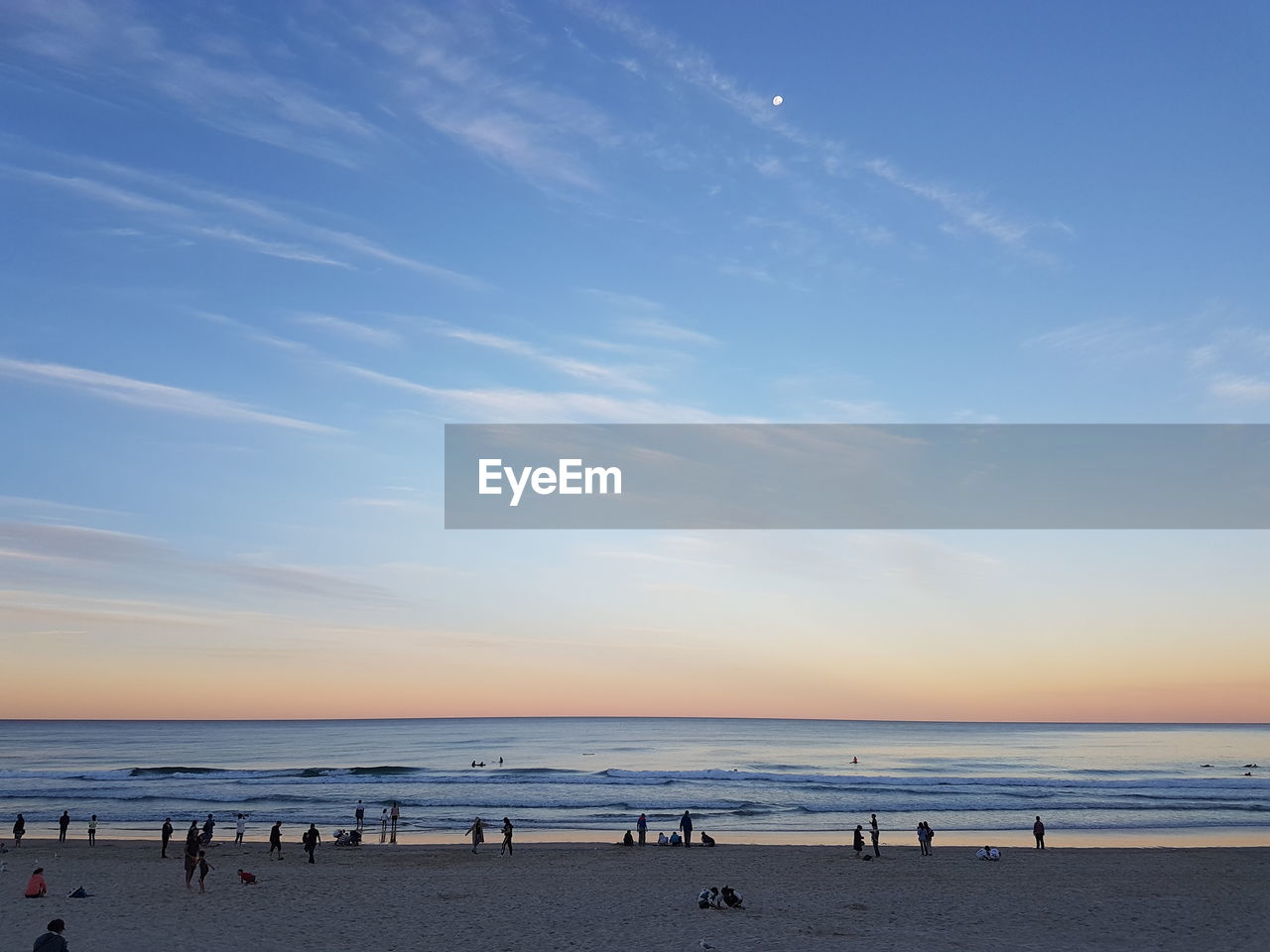 People at beach against sky during sunset