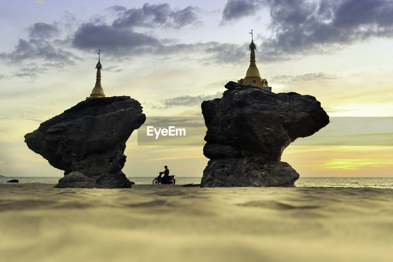 STATUE ON ROCK FORMATION AT BEACH AGAINST SKY