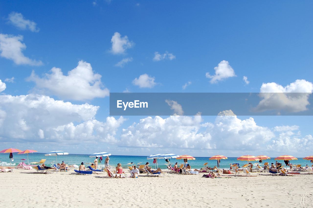 People on sandy beach against blue sky