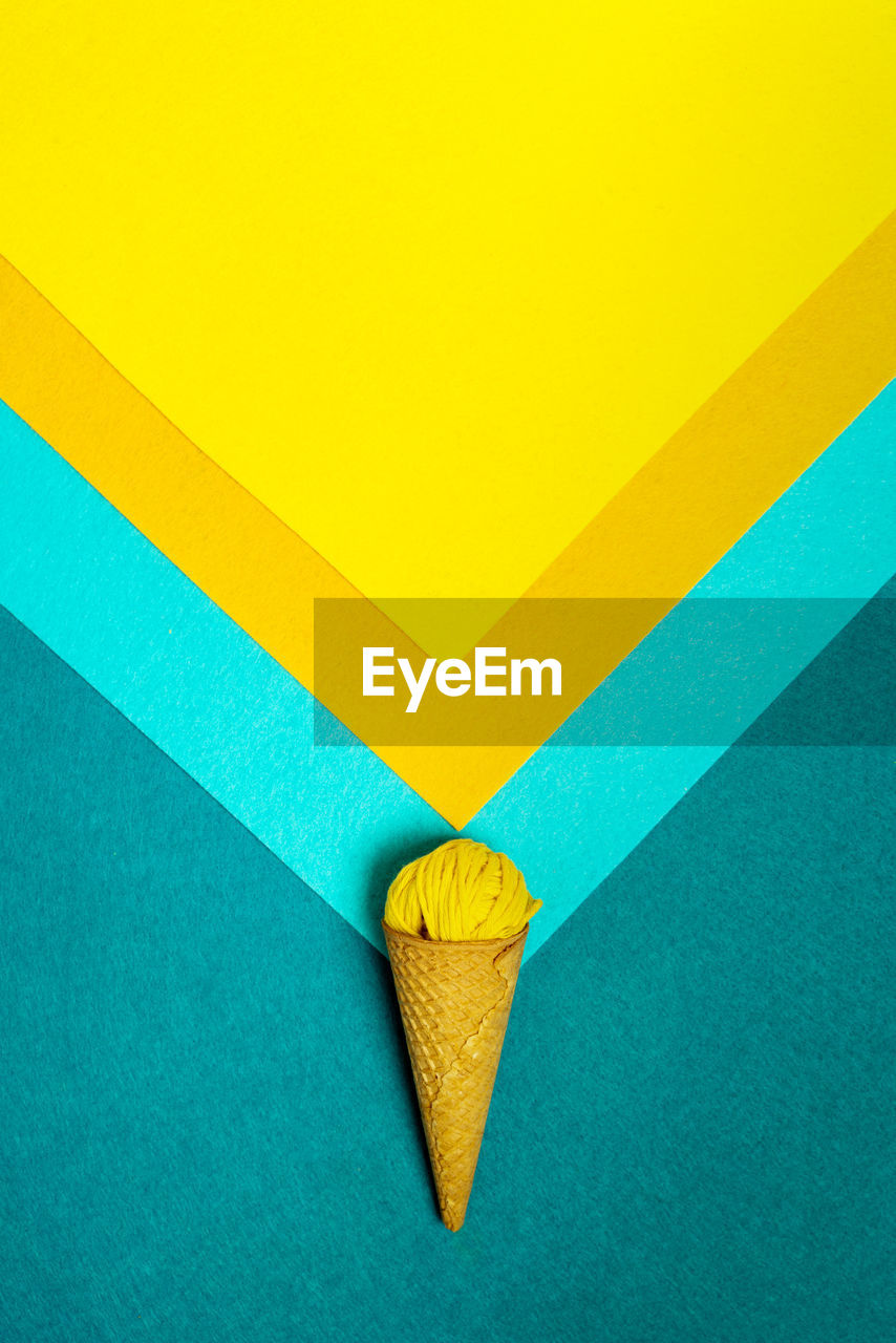 From above of crunchy waffle cone with small woolen thread ball representing ice cream on colorful background