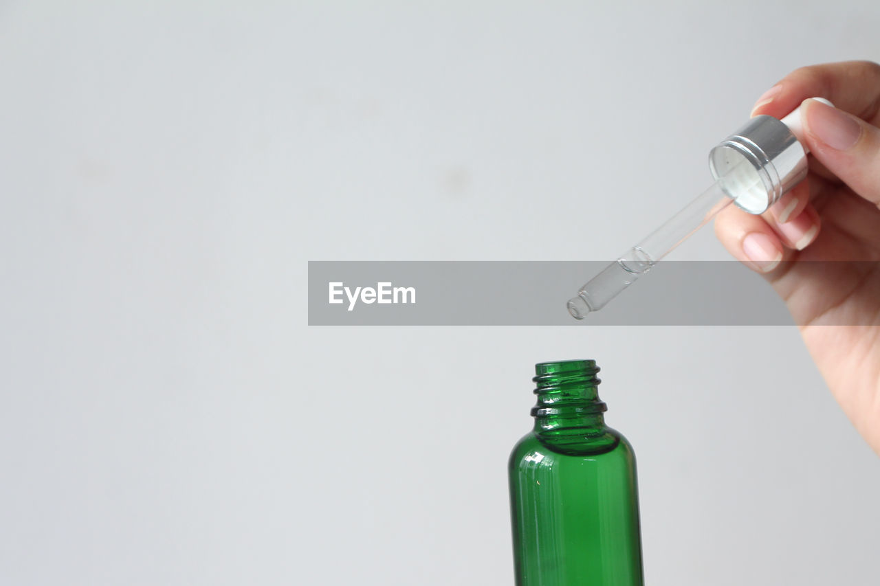 Woman hands holding facial essential oil or serum packaging on white background. 