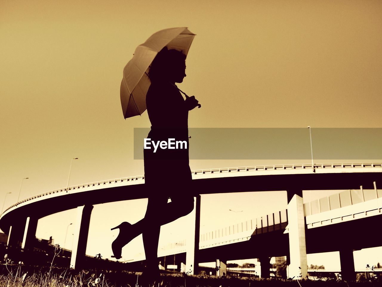 Full length of silhouette woman with umbrella standing by bridge against clear sky