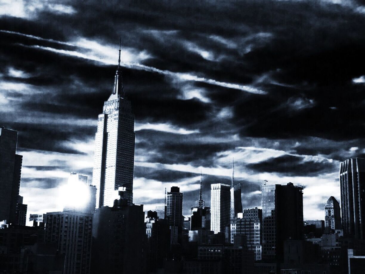 Low angle view of empire state building amidst buildings in city against cloudy sky