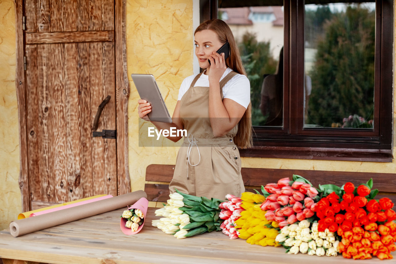 A young female florist with a tablet in her hands is talking on the phone and making an order 