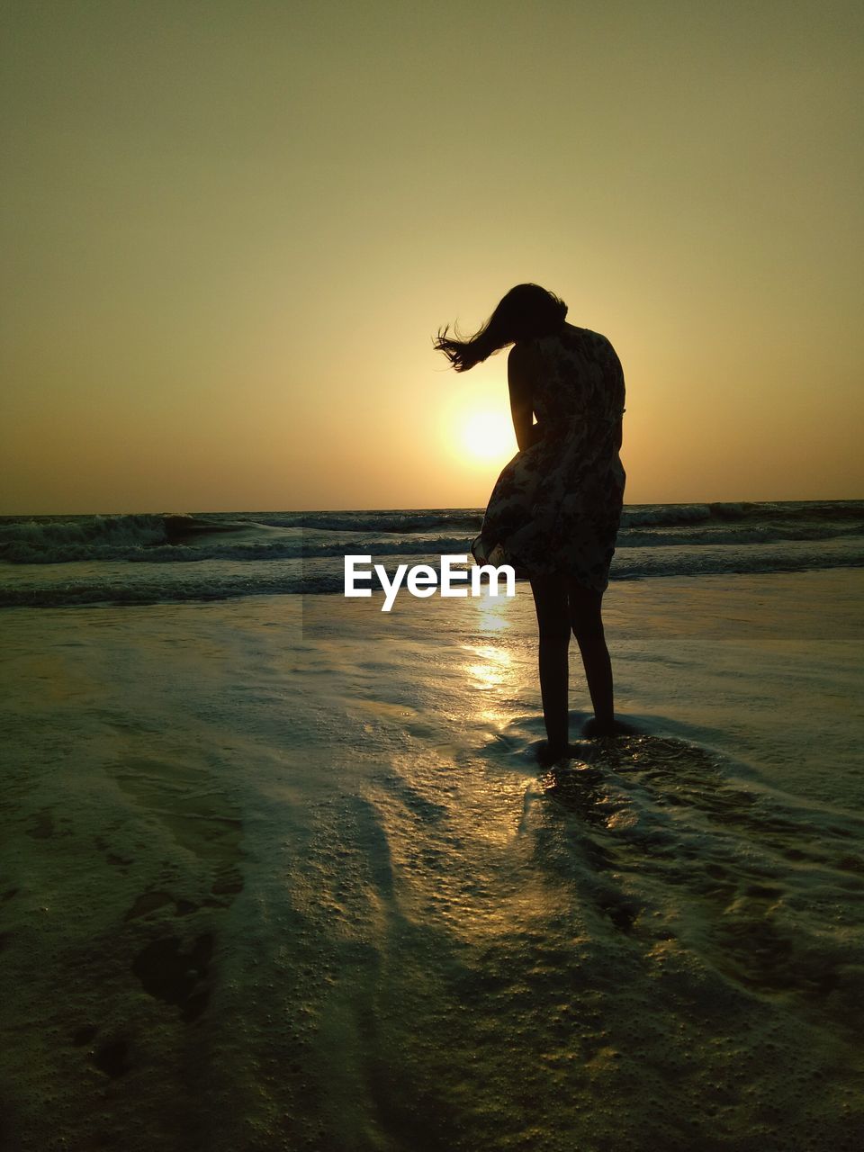 Full length of woman standing in sea against sky during sunset