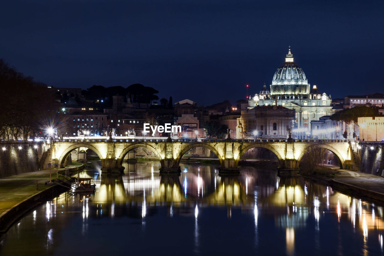 Illuminated bridge over river against buildings at night