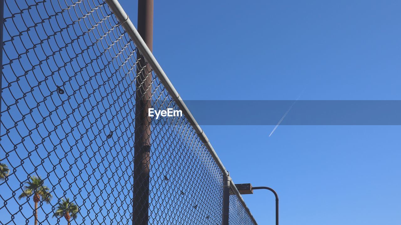 LOW ANGLE VIEW OF METALLIC FENCE AGAINST CLEAR BLUE SKY