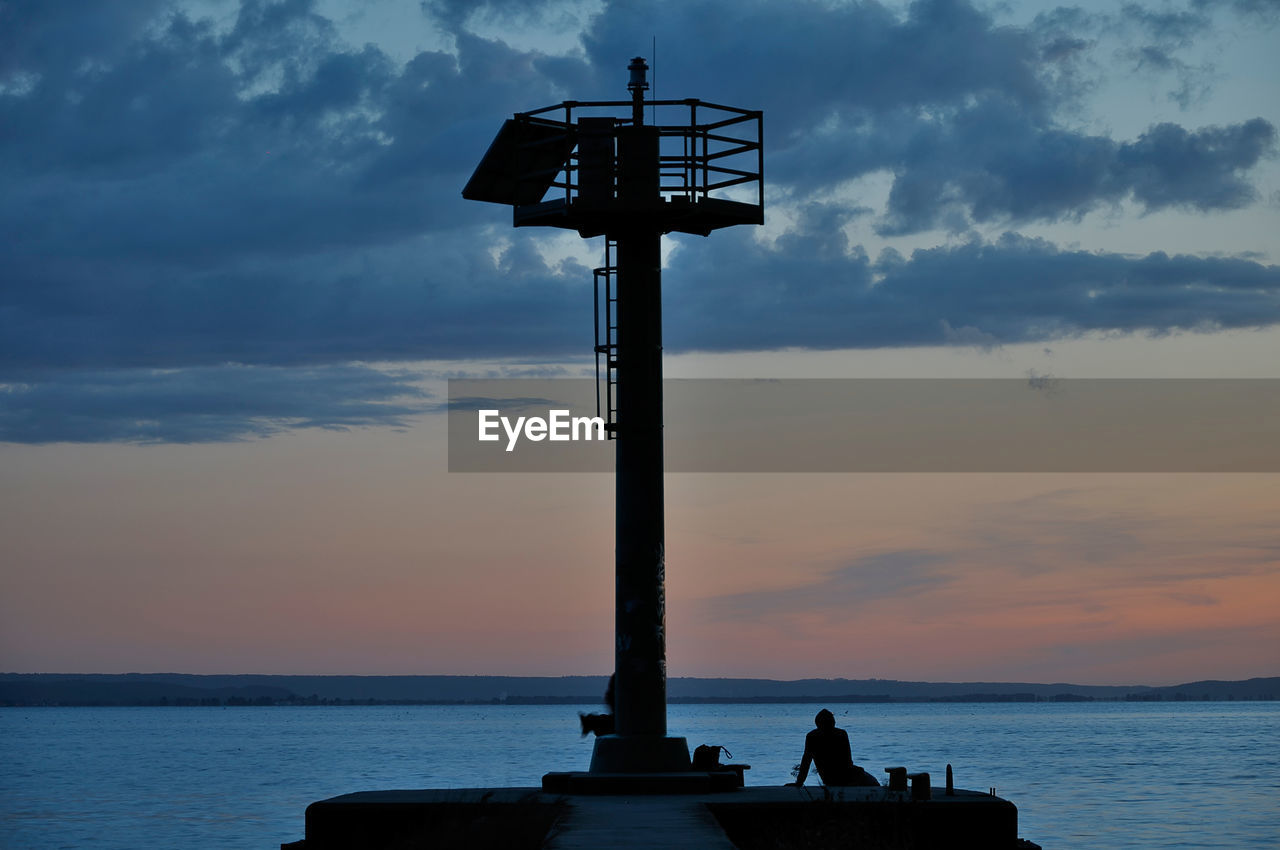 Silhouette cross by sea against sky at sunset