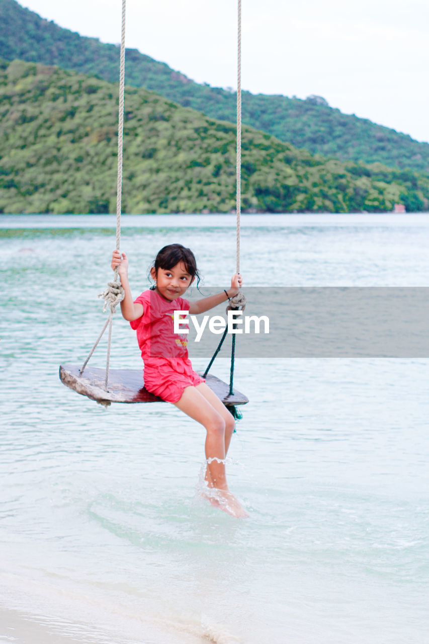 Full length of little girl on swing in sea