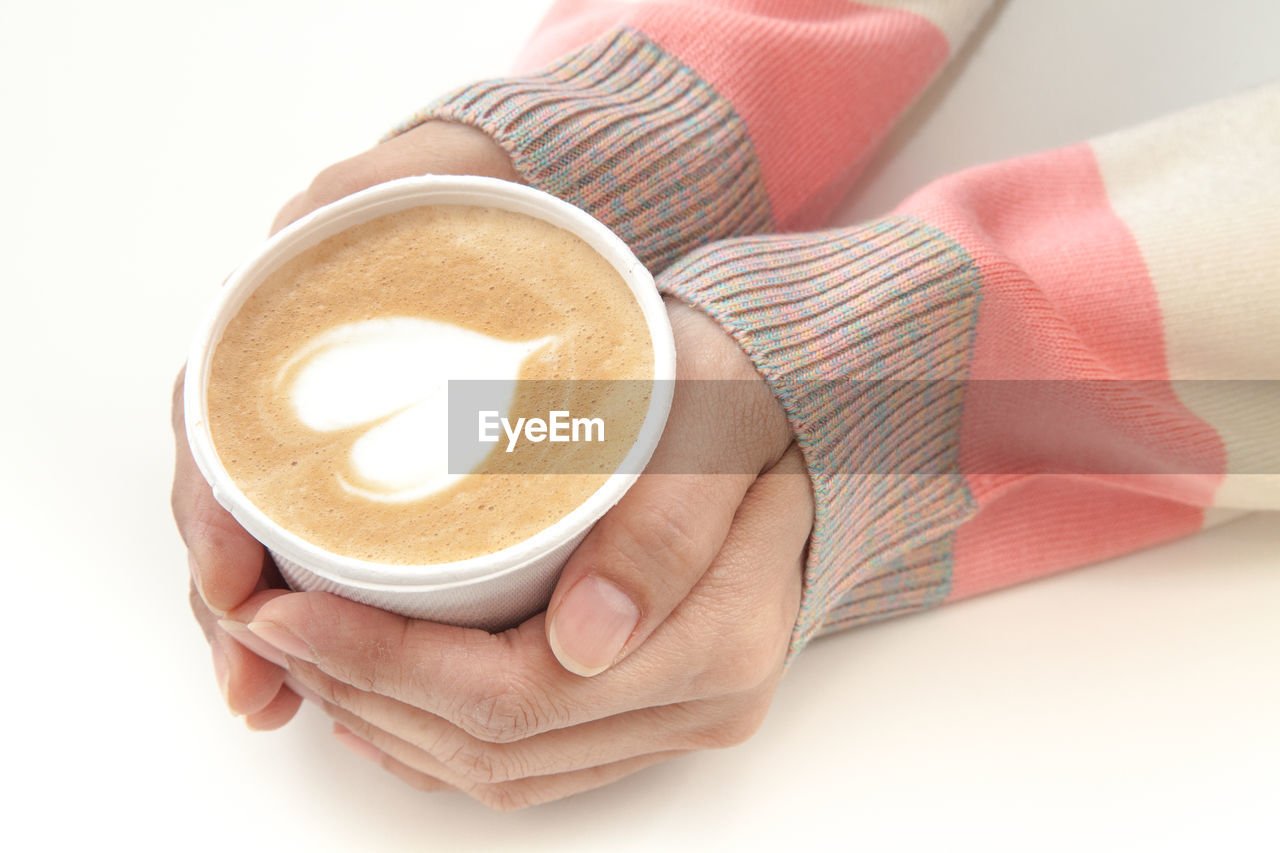 Cropped hands of woman holding cappuccino over white background