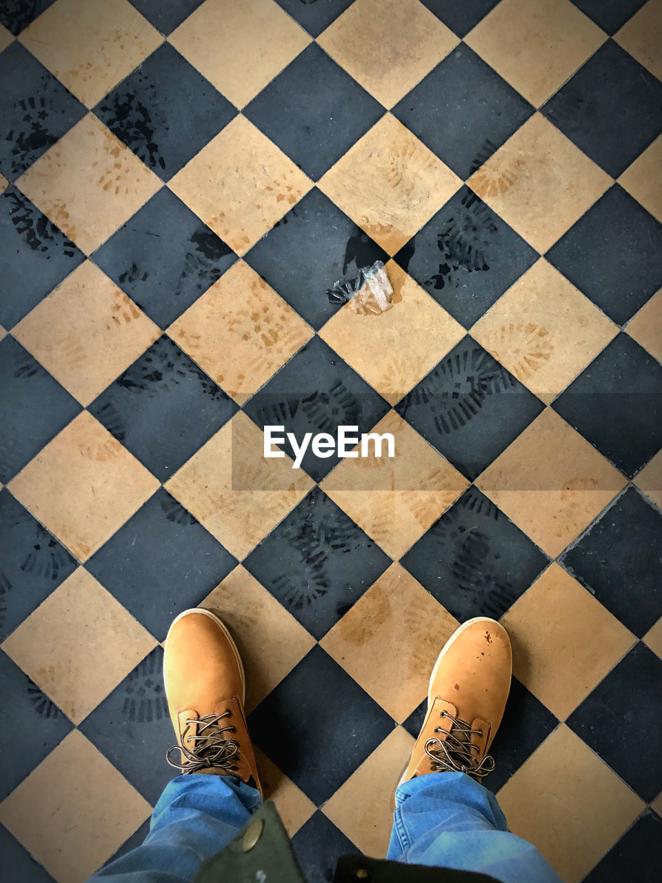 Low section body of a man with blue jeans and winter boots on a tiled checkerboard pattern floor