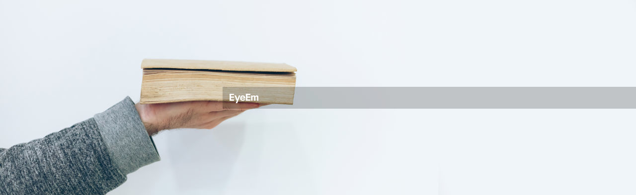 CLOSE-UP OF HAND HOLDING BOOK OVER WHITE BACKGROUND