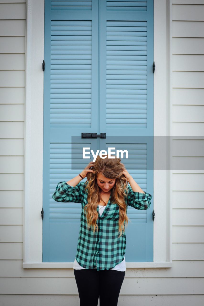 Young woman wearing checked pattern shirt with hand in hair standing against close window