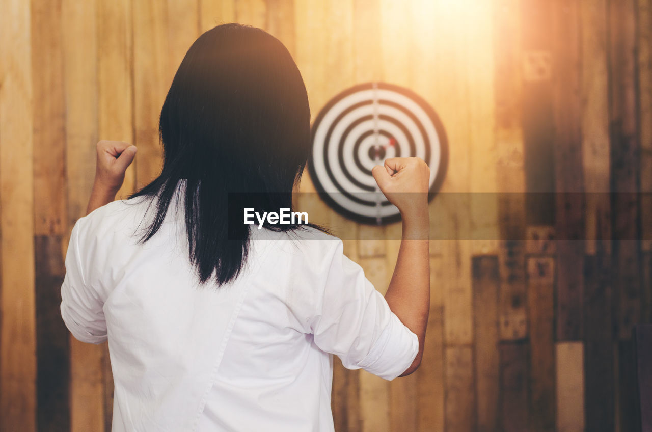 Woman clenching fists while standing against dartboard