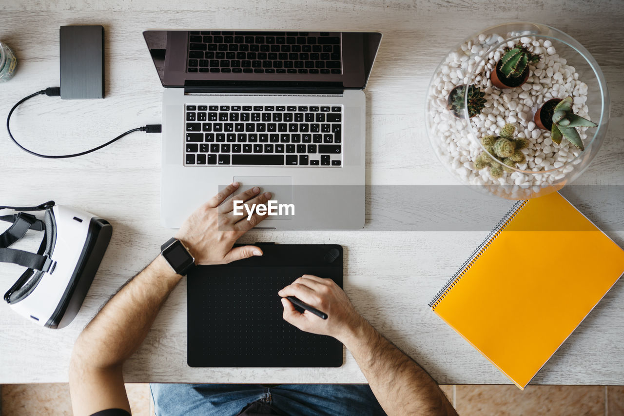 Man working with graphics tablet and laptop at home office, top view