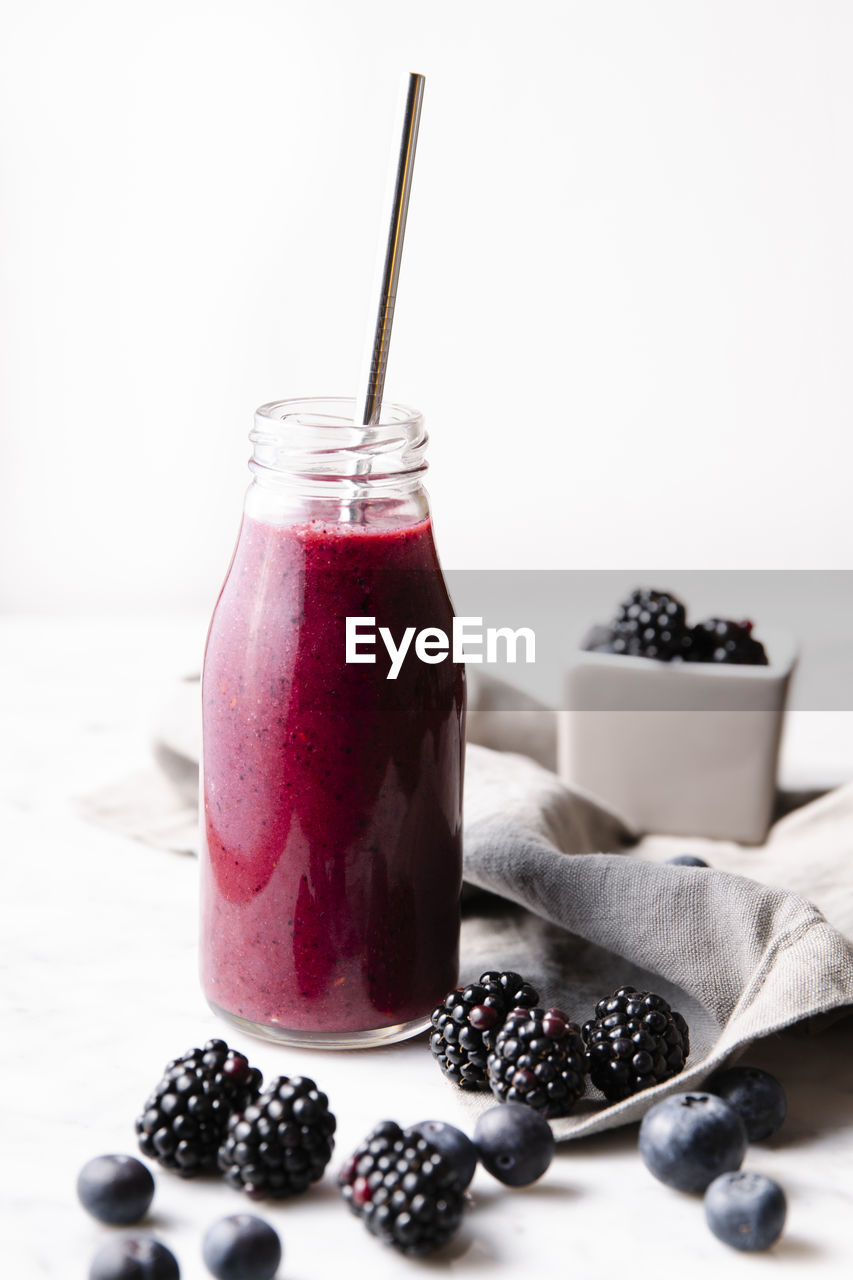 Front shot of a glass bottle with berry smoothie, with a metal straw in it. vertical image.