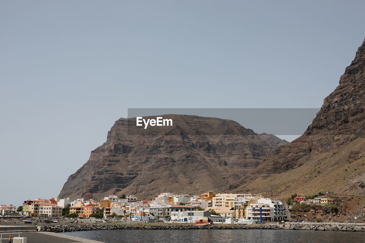 Buildings by mountain against clear sky