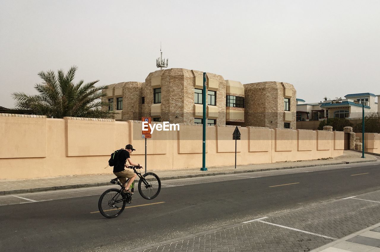 MAN CYCLING ON BICYCLE AGAINST CLEAR SKY