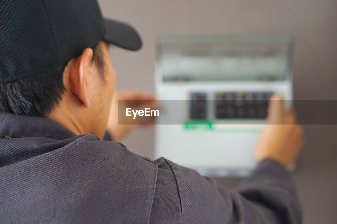 Rear view of man working on electrical equipment