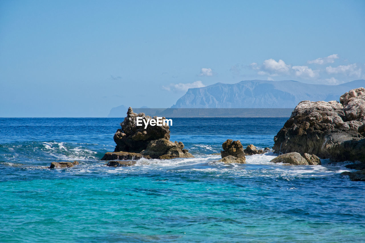 Rock formation in sea against blue sky