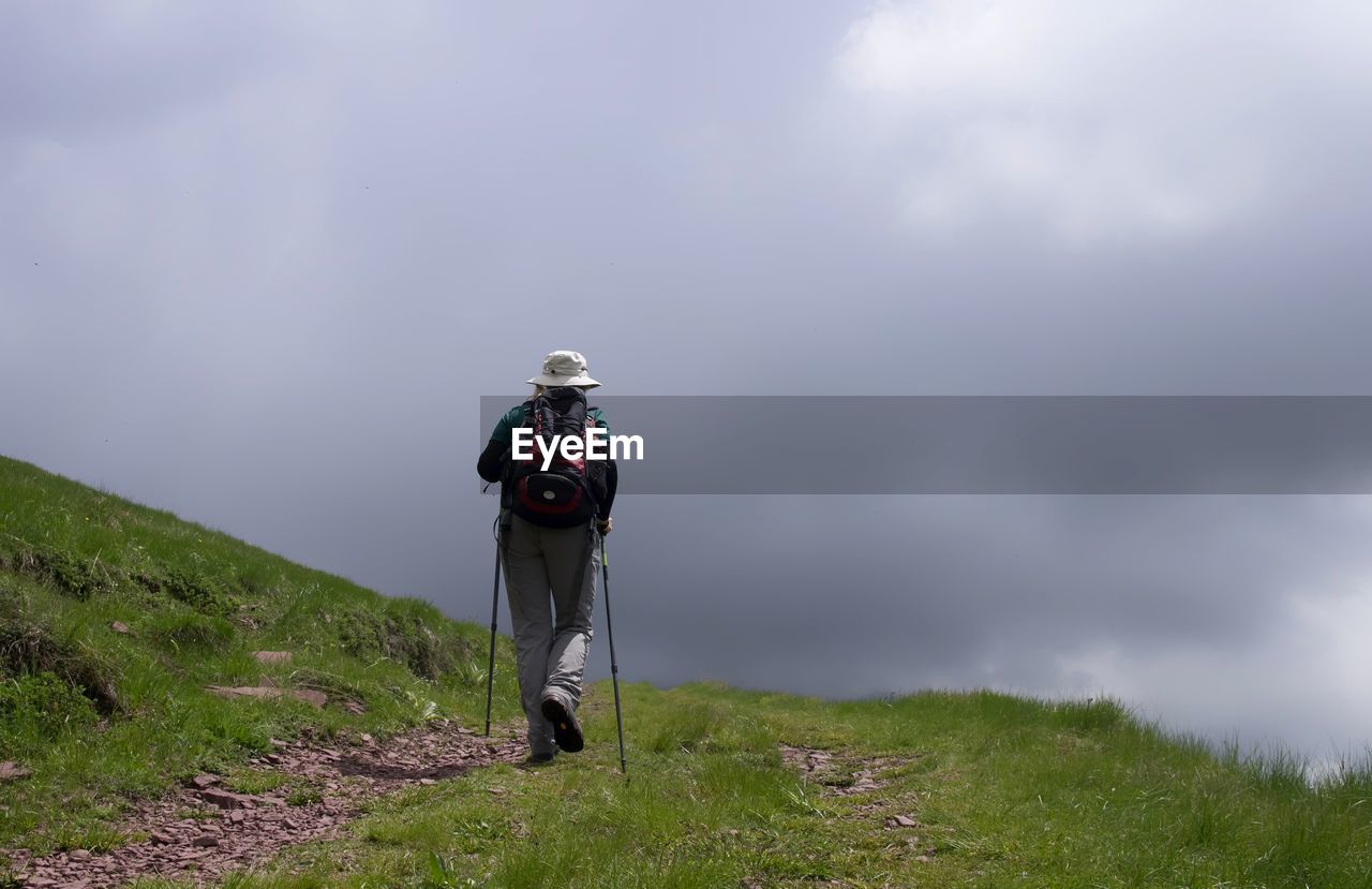 Rear view of woman standing on grass against sky