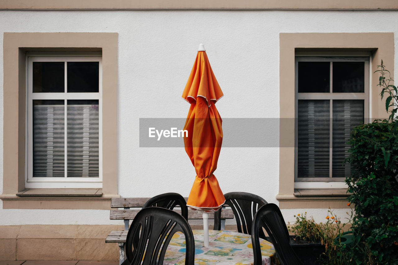 Closed orange parasol in front of wall with windows