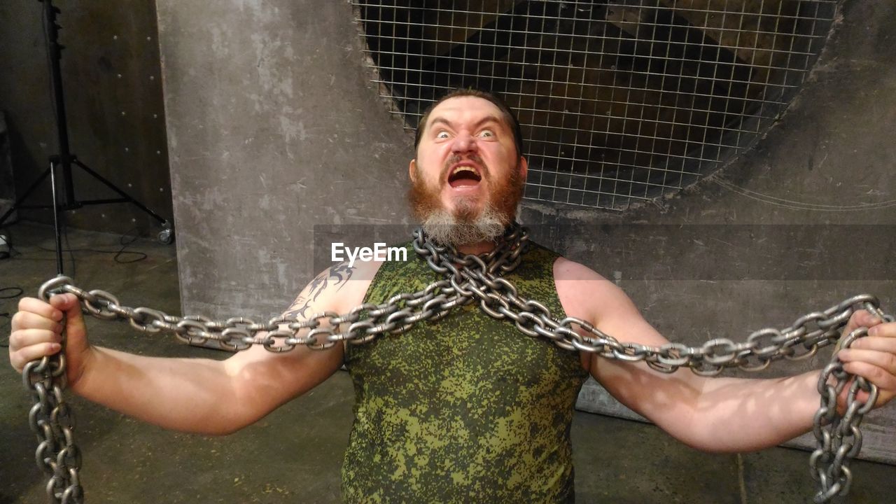 Portrait of mid adult man with chain screaming while standing against metal