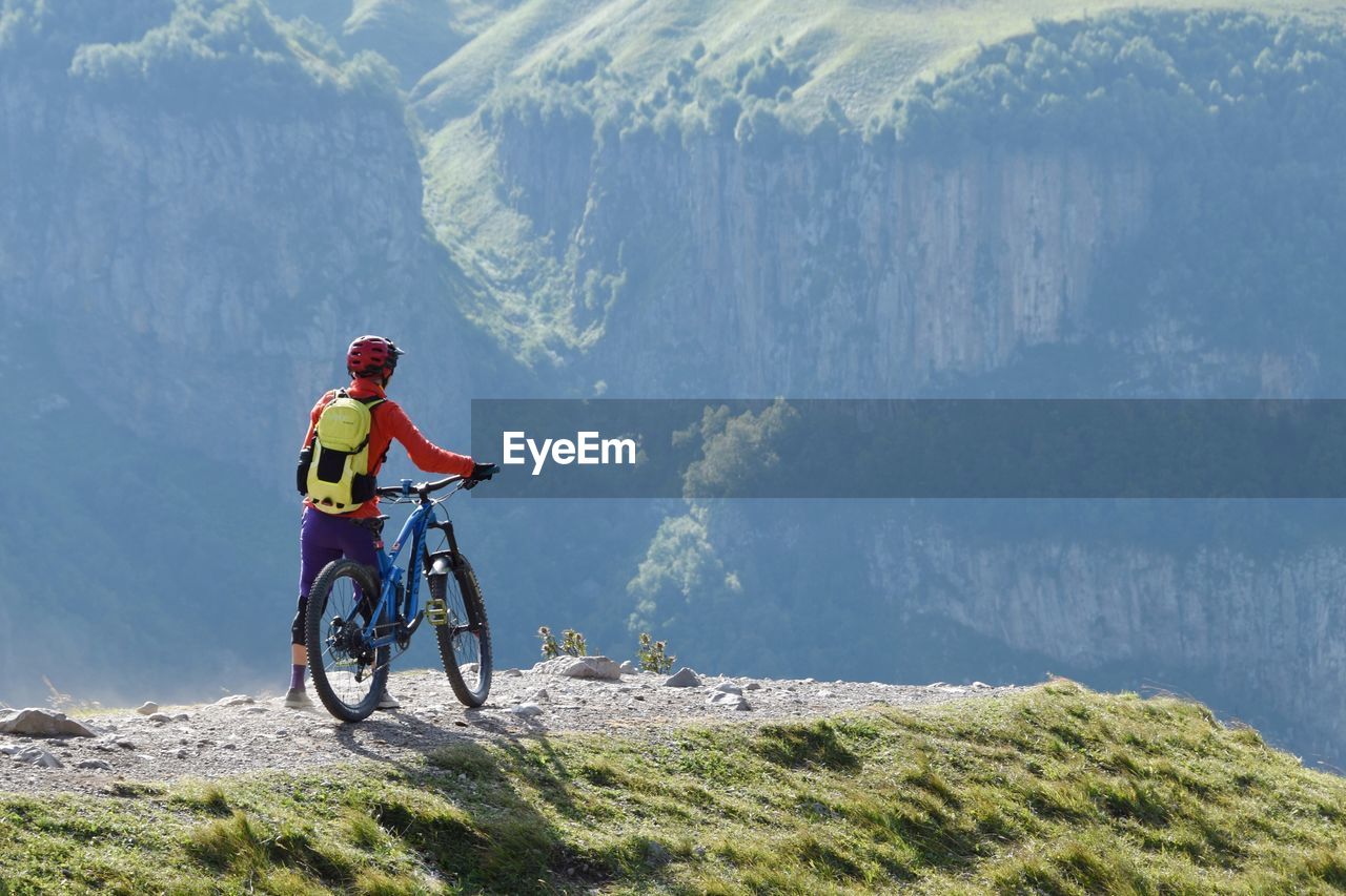 Rear view of man with bicycle standing on mountain peak
