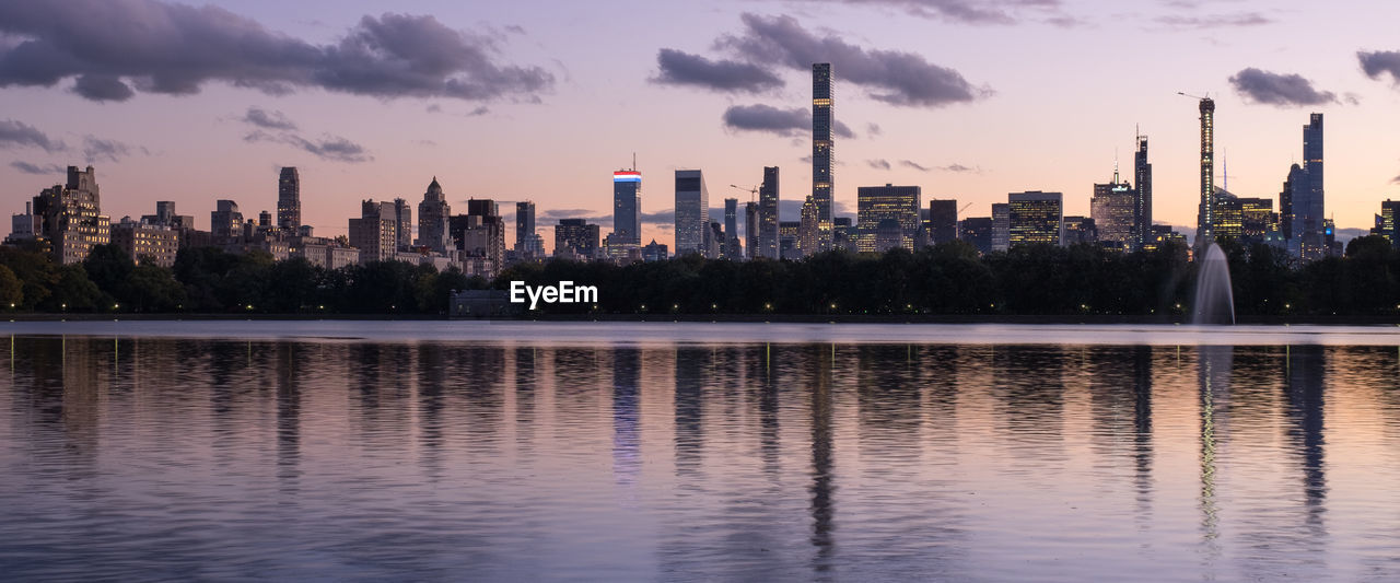 Scenic view of lake by buildings against sky during sunset