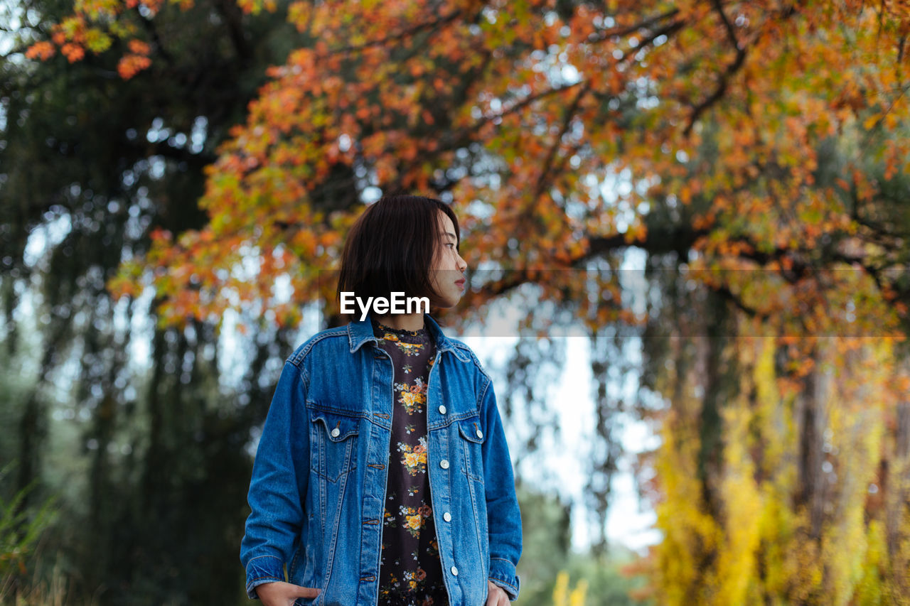 Mid adult woman looking away while standing against autumn trees