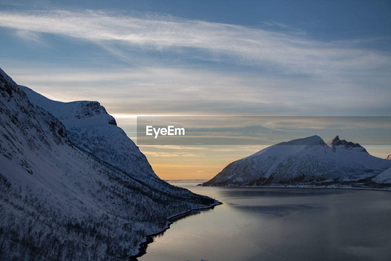 Scenic view of sea by snowcapped mountains against sky during sunset