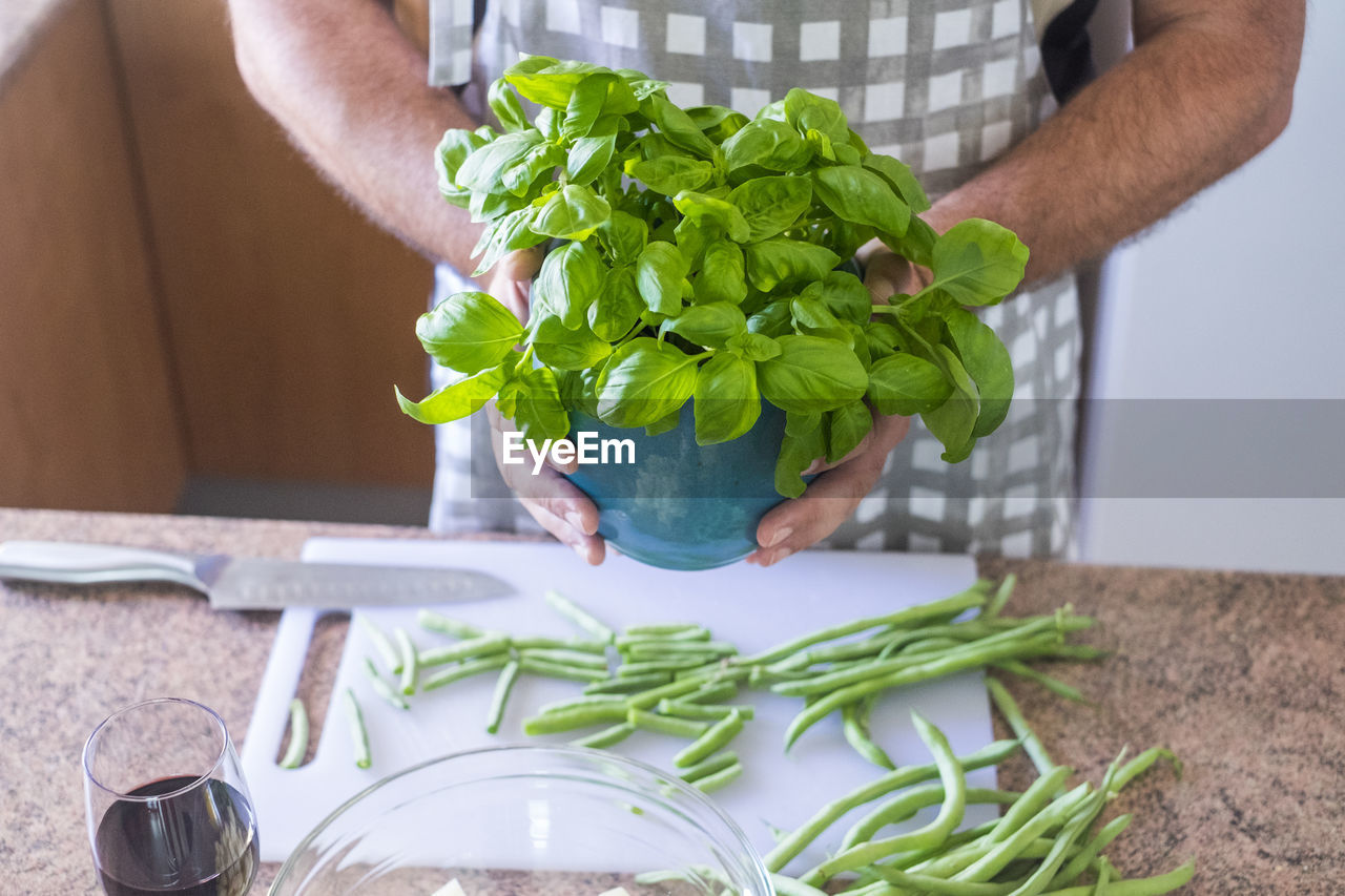 Midsection of man holding potted plant while preparing food in kitchen at home