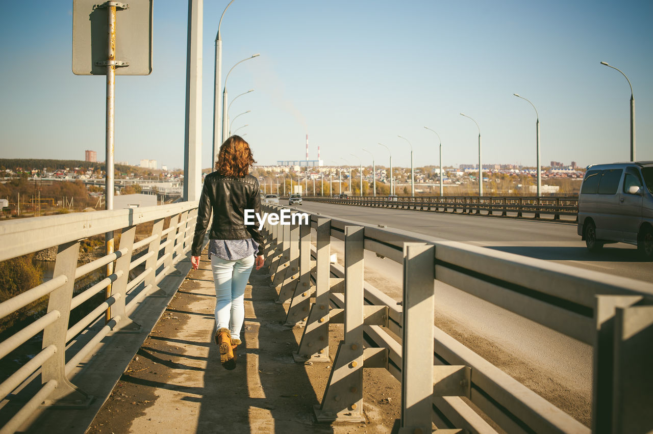 Rear view of young woman walking on bridge against sky