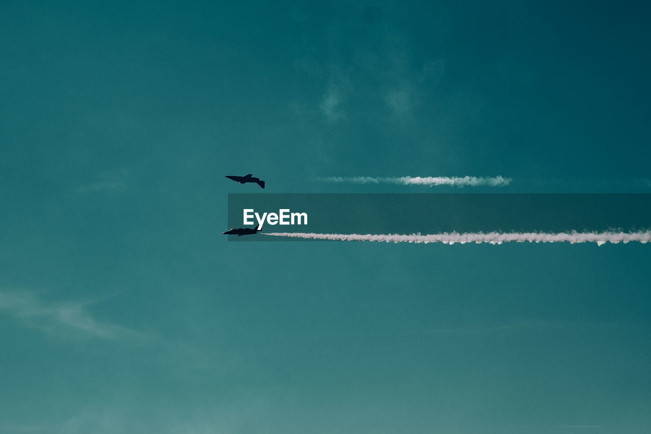 Low angle view of airplanes flying against blue sky