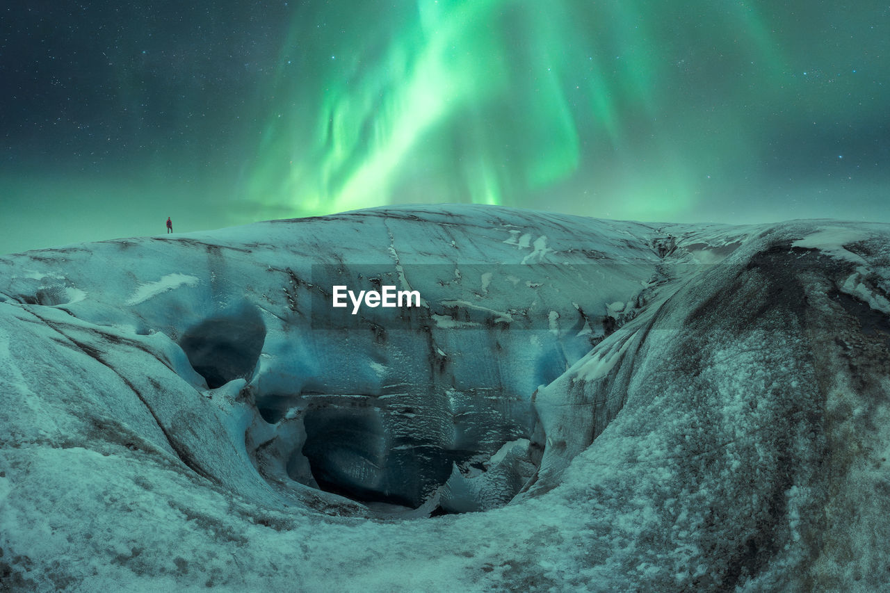 Uneven ice formation of vatnajokull glacier with tourist located against night sky with bright green aurora borealis on winter day in iceland