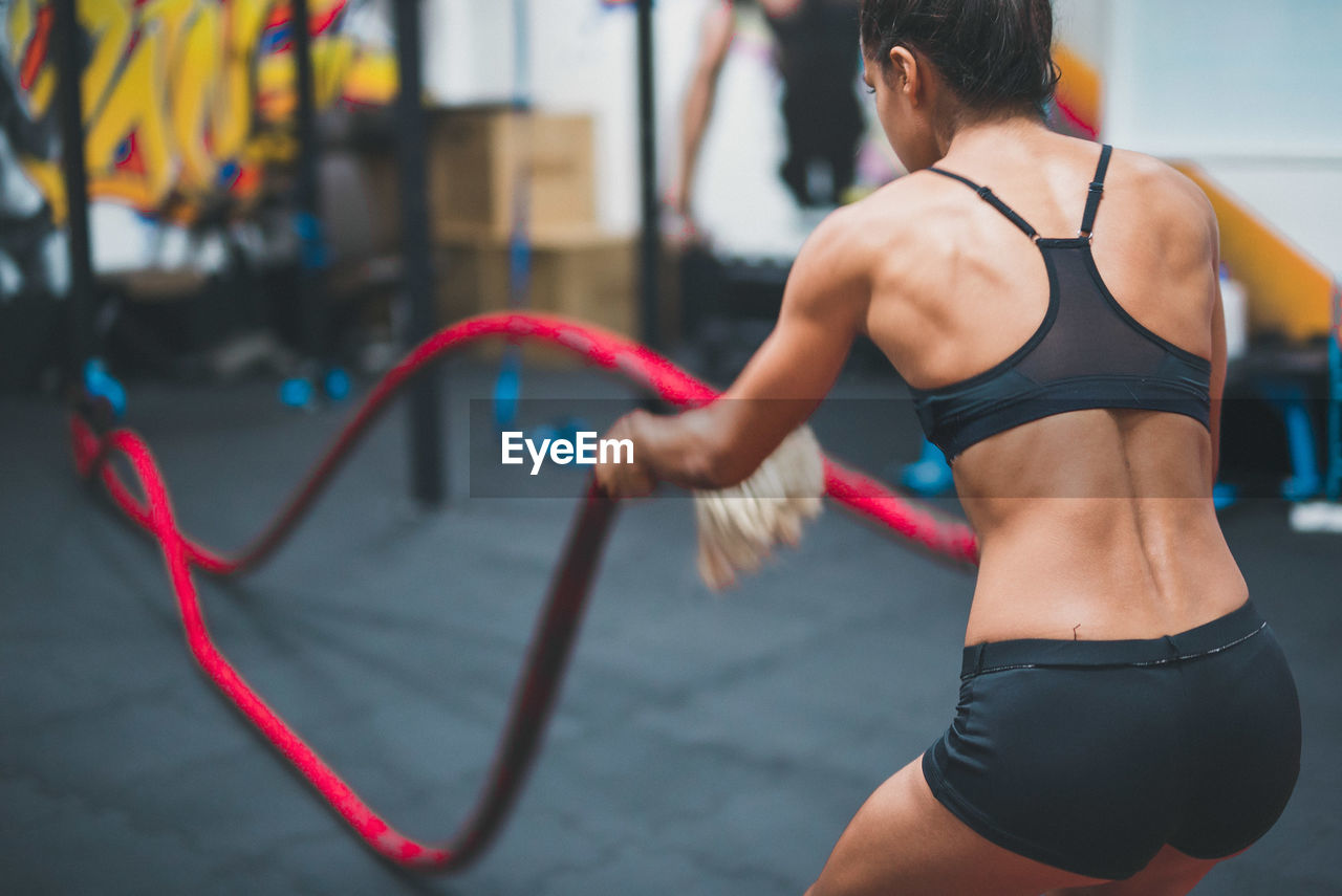 Rear view of female athlete exercising battle rope in gym