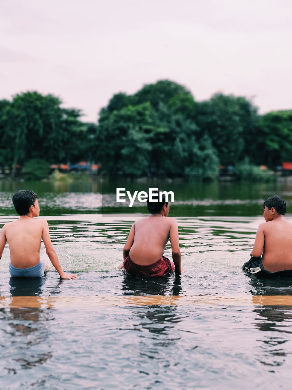 Rear view of boys sitting by lake