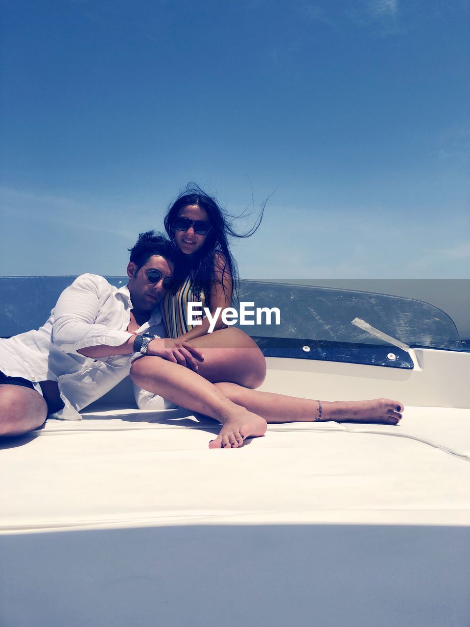 Young coupe sitting on boat at sea against sky