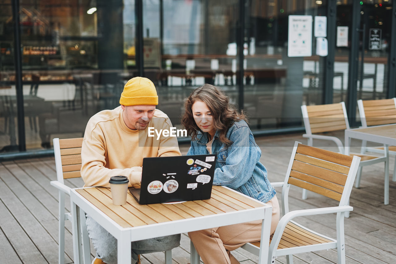 Stylish young couple freelancers working on laptop in street cafe