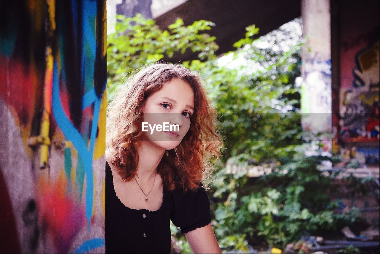 Portrait of a pretty young woman sitting close to a graffiti wall 