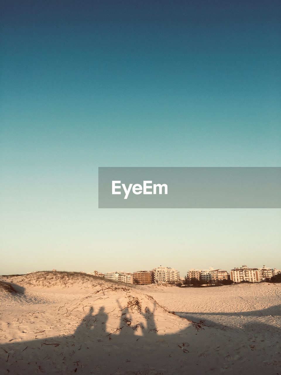 Shadow on people at beach against buildings and sky