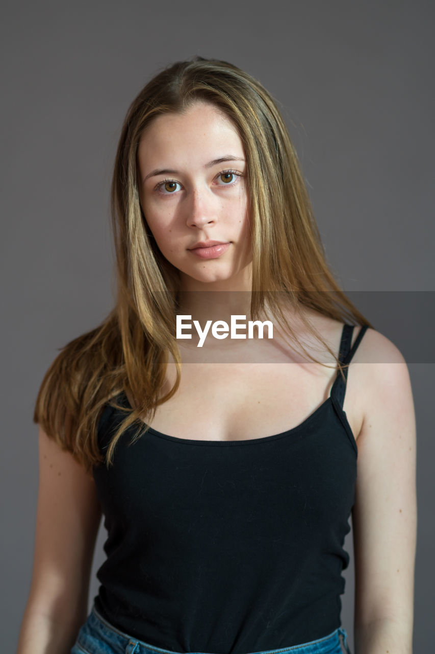 Portrait of an attractive teenage girl wearing a camisole looking at camera on grey background