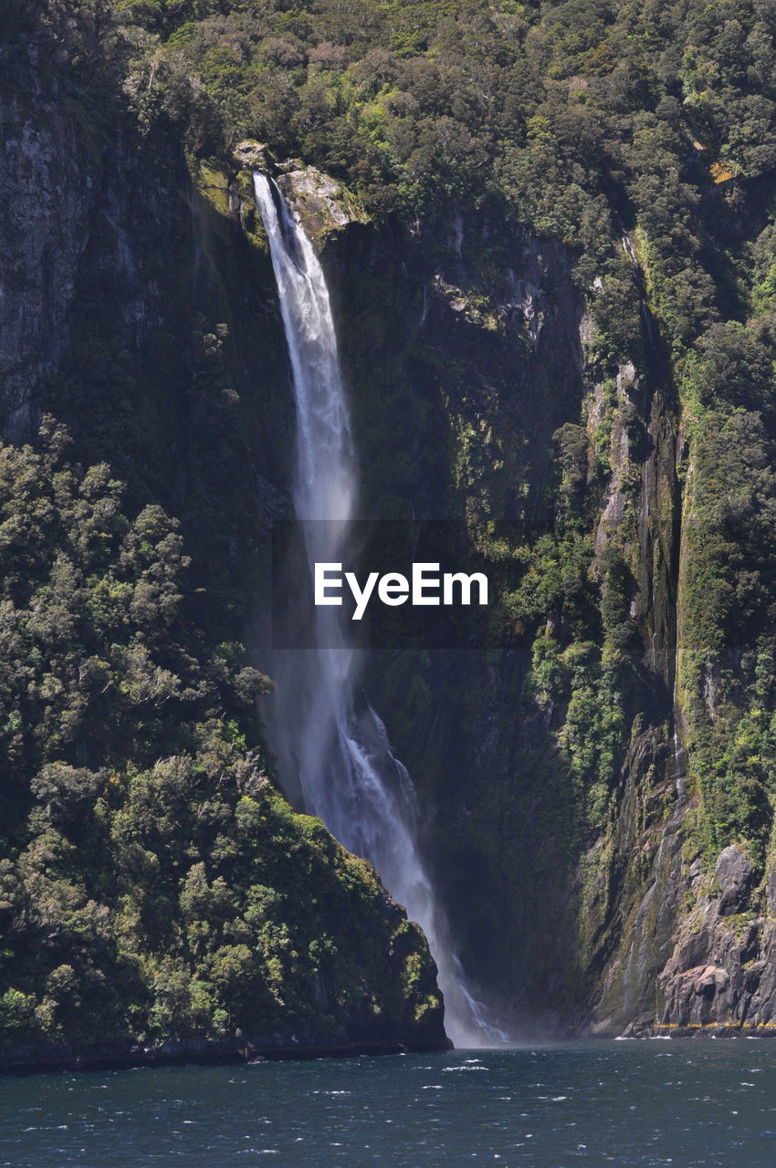 SCENIC VIEW OF WATERFALL BY SEA AGAINST MOUNTAIN