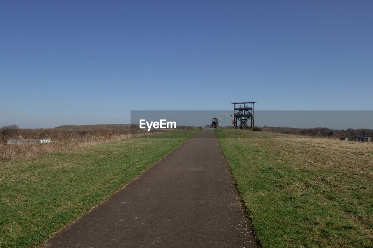 sky, hill, horizon, rural area, landscape, nature, road, environment, clear sky, grass, architecture, prairie, blue, land, no people, transportation, field, built structure, rural scene, scenics - nature, infrastructure, coast, plant, the way forward, tranquility, plain, day, outdoors, non-urban scene, tranquil scene, copy space, sea, travel, beauty in nature