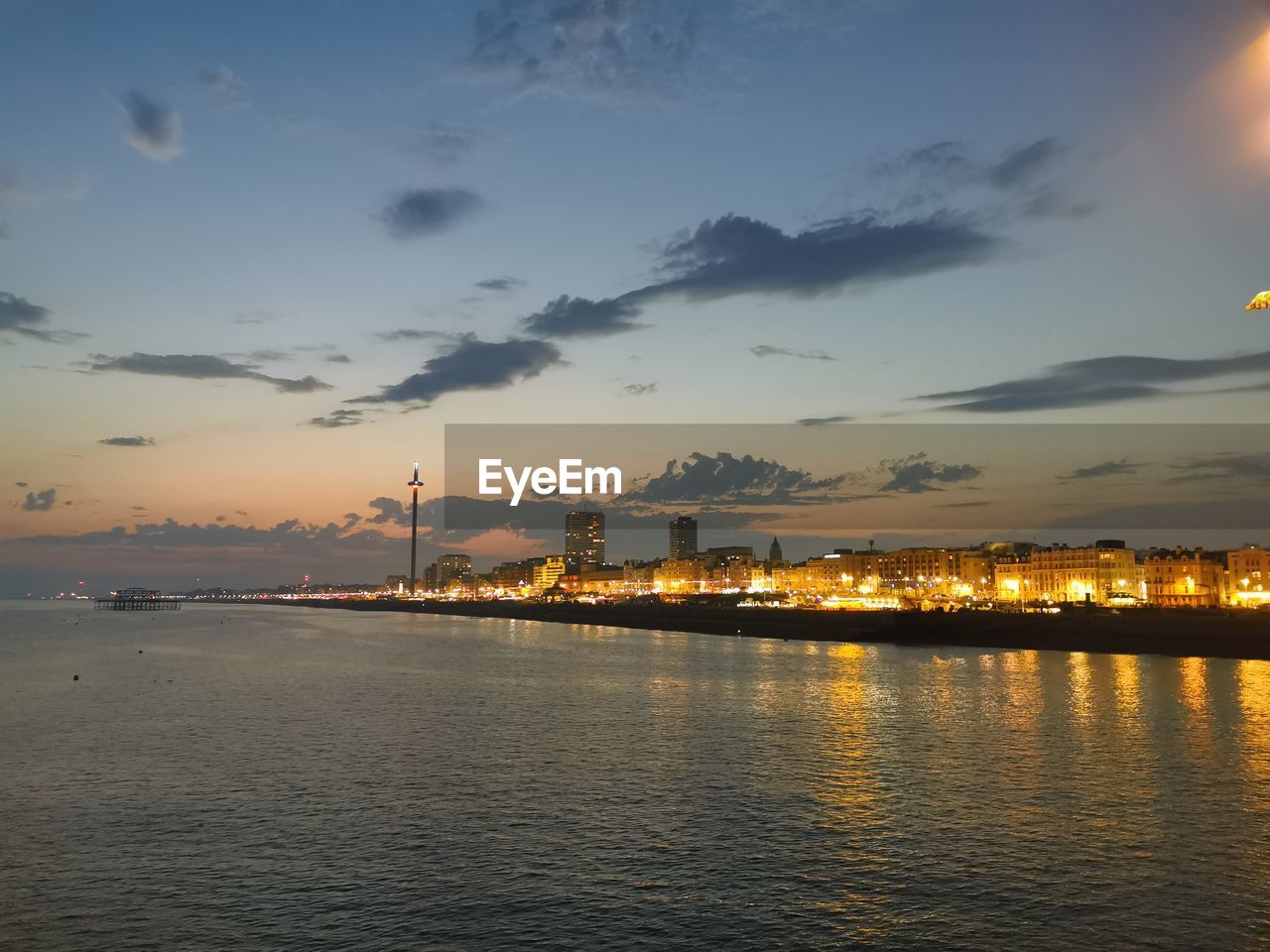 Illuminated city by sea against sky during sunset