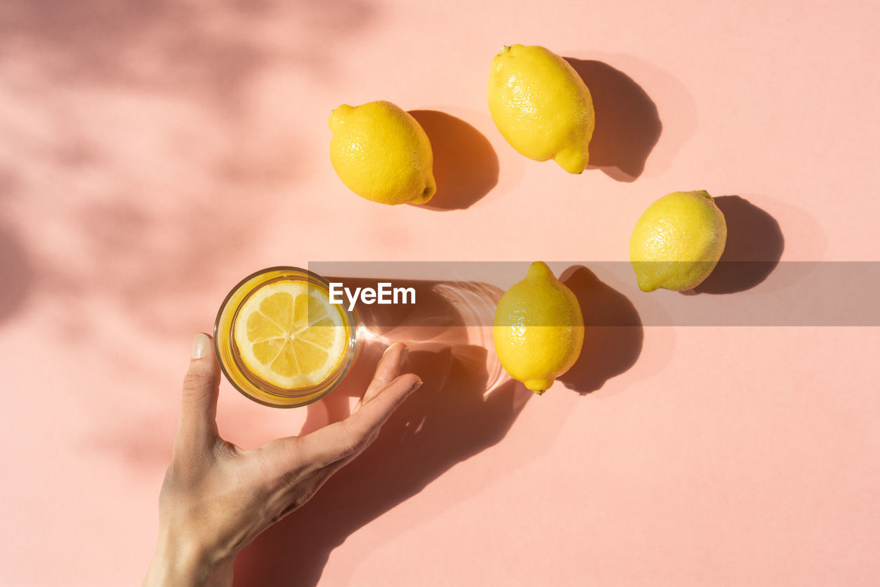 Close-up of hand with drinking glass and lemons on pink background