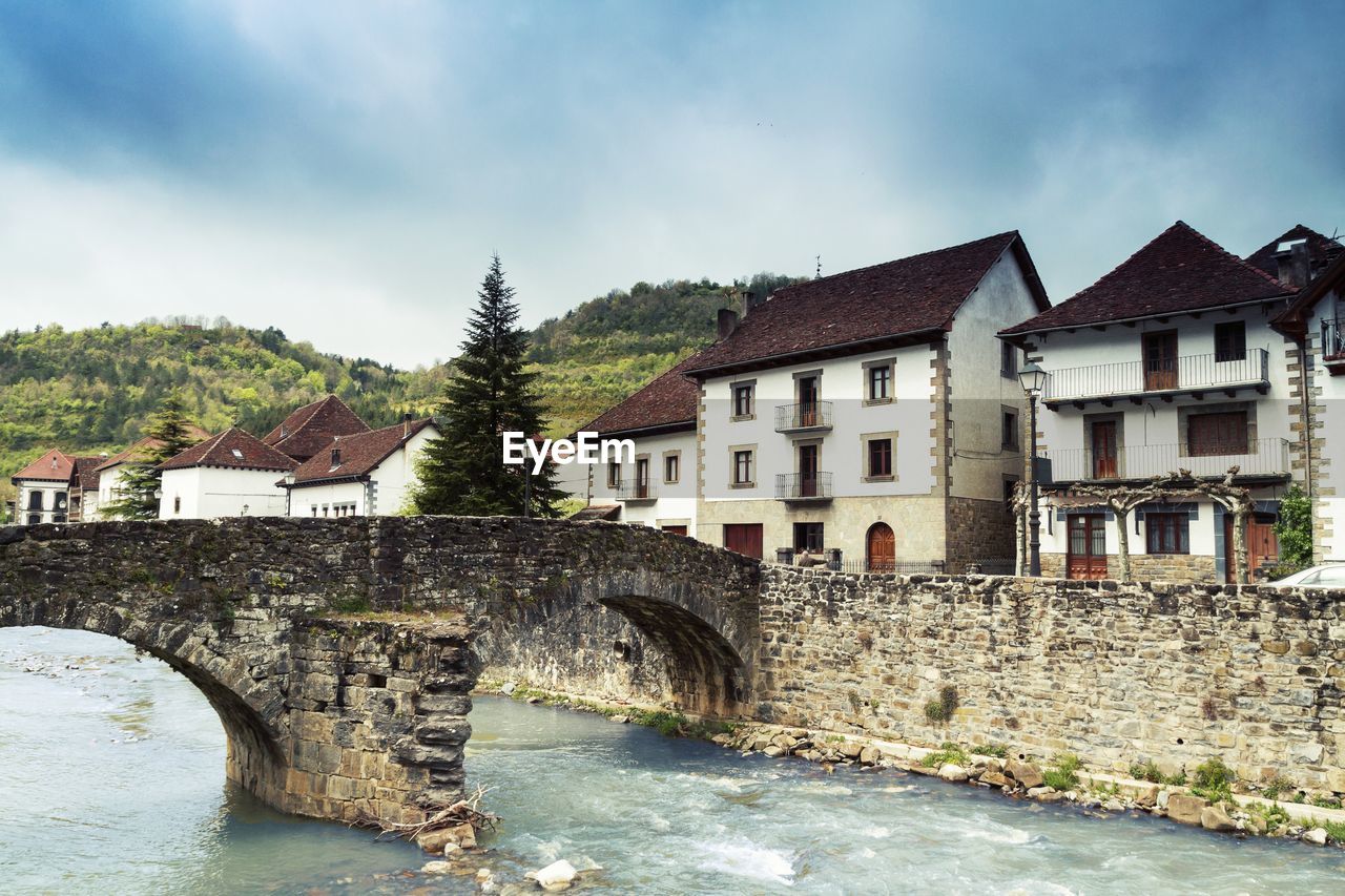 ARCH BRIDGE OVER RIVER AMIDST BUILDINGS